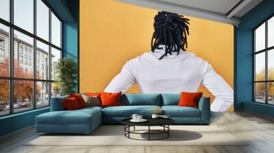 African man with dreadlocks wearing turtleneck sweater over yellow background standing backwards looking away with arms on body Wall mural