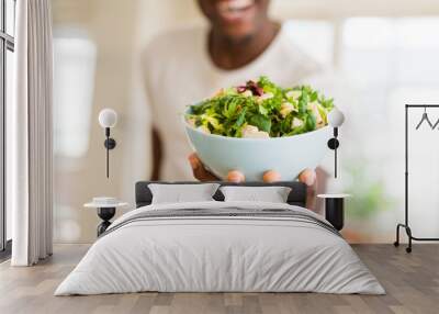 African young man holding a bowl of healthy salad smiling cheerful Wall mural