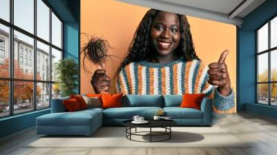 African young woman holding comb loosing hair smiling happy and positive, thumb up doing excellent and approval sign Wall mural