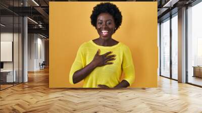 African young woman standing over yellow studio smiling and laughing hard out loud because funny crazy joke with hands on body. Wall mural