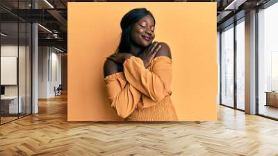 African young woman wearing casual clothes hugging oneself happy and positive, smiling confident. self love and self care Wall mural