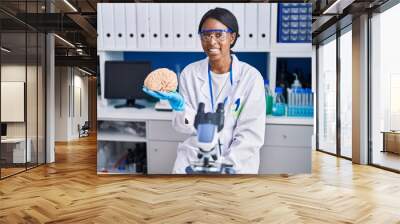 African young woman working at scientist laboratory holding brain looking positive and happy standing and smiling with a confident smile showing teeth Wall mural