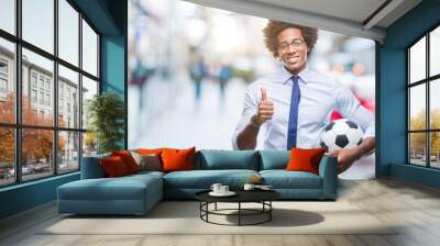 Afro american manager man holding soccer ball over isolated background happy with big smile doing ok sign, thumb up with fingers, excellent sign Wall mural