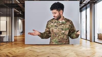 Arab man wearing camouflage army uniform smiling showing both hands open palms, presenting and advertising comparison and balance Wall mural