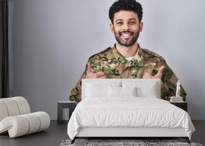 Arab man wearing camouflage army uniform success sign doing positive gesture with hand, thumbs up smiling and happy. cheerful expression and winner gesture. Wall mural