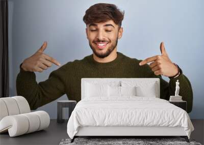 Arab man with beard standing over blue background looking confident with smile on face, pointing oneself with fingers proud and happy. Wall mural