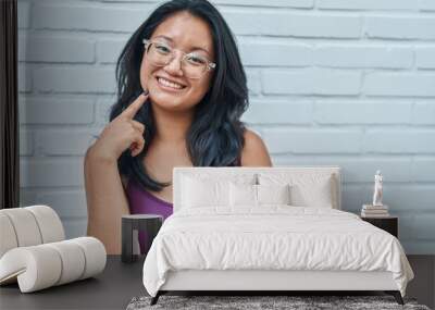 Asian young woman standing over bricks background smiling happy pointing with hand and finger Wall mural