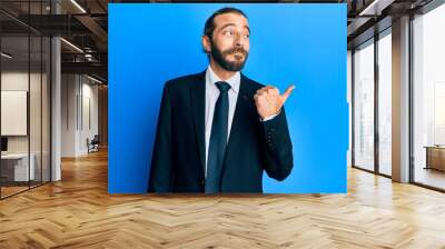 Attractive man with long hair and beard wearing business suit and tie smiling with happy face looking and pointing to the side with thumb up. Wall mural