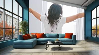 Back view of a brunette woman stretching arms in a bright bedroom, suggesting a morning routine. Wall mural