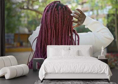 Back view of a young african american woman with burgundy braids in a park setting touching her hair. Wall mural