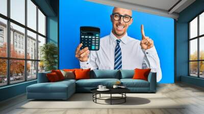 Bald business man with beard showing calculator device smiling with an idea or question pointing finger with happy face, number one Wall mural