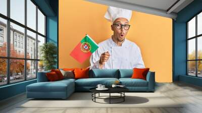 Bald man with beard wearing professional cook apron holding portugal flag scared and amazed with open mouth for surprise, disbelief face Wall mural