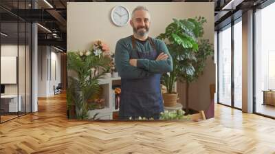 Bearded man in apron smiling confidently at a vibrant indoor flower shop with lush green plants Wall mural