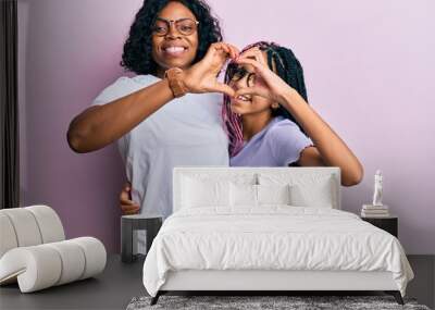 Beautiful african american mother and daughter wearing casual clothes and glasses doing heart shape with hand and fingers smiling looking through sign Wall mural