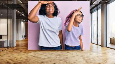 Beautiful african american mother and daughter wearing casual clothes and glasses very happy and smiling looking far away with hand over head. searching concept. Wall mural