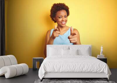 Beautiful african american woman wearing elegant shirt over isolated yellow background pointing fingers to camera with happy and funny face. Good energy and vibes. Wall mural