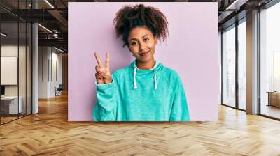 Beautiful african american woman with afro hair wearing casual sweatshirt smiling with happy face winking at the camera doing victory sign. number two. Wall mural