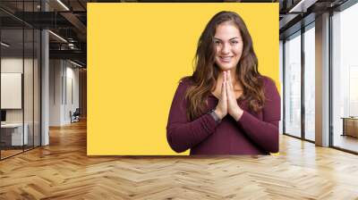 Beautiful and attractive plus size young woman wearing a dress over isolated background praying with hands together asking for forgiveness smiling confident. Wall mural