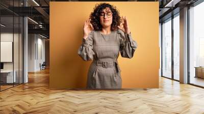 Beautiful arab business woman wearing dress and glasses standing over yellow background relaxed and smiling with eyes closed doing meditation gesture with fingers. Yoga concept. Wall mural