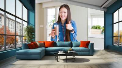 Beautiful Asian woman drinking a fresh glass of chocolate milkshake happy with big smile doing ok sign, thumb up with fingers, excellent sign Wall mural