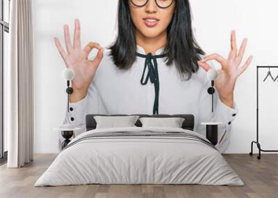 Beautiful asian young woman wearing business shirt and glasses relax and smiling with eyes closed doing meditation gesture with fingers. yoga concept. Wall mural