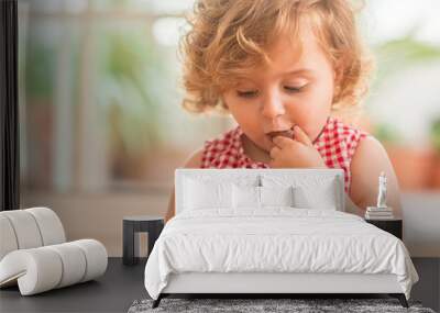 Beautiful blonde child with blue eyes eating candy at home. Wall mural