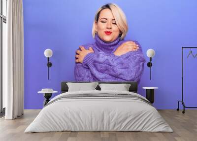 Beautiful blonde plus size woman wearing casual turtleneck sweater over purple background Hugging oneself happy and positive, smiling confident. Self love and self care Wall mural