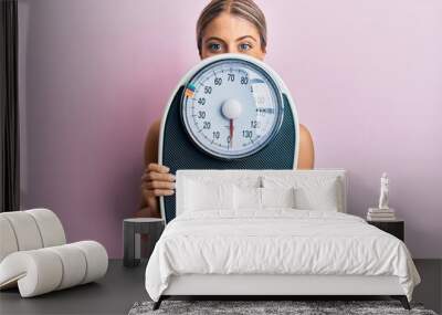 Beautiful blonde woman holding weight machine to balance weight loss smiling with a happy and cool smile on face. showing teeth. Wall mural