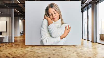 Beautiful blonde woman wearing casual turtleneck sweater hugging oneself happy and positive, smiling confident. self love and self care Wall mural