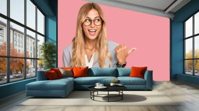 Beautiful blonde young woman wearing business clothes smiling with happy face looking and pointing to the side with thumb up. Wall mural