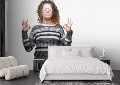 Beautiful brunette curly hair young girl wearing glasses over isolated background relax and smiling with eyes closed doing meditation gesture with fingers. Yoga concept. Wall mural