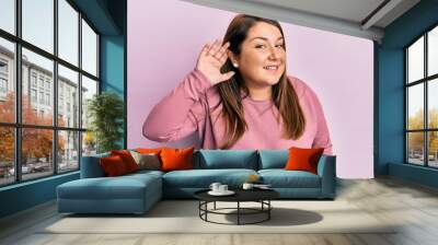 Beautiful brunette plus size woman wearing casual winter sweater smiling with hand over ear listening and hearing to rumor or gossip. deafness concept. Wall mural