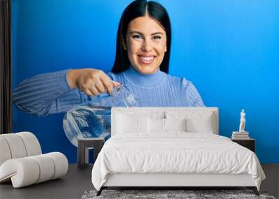 Beautiful brunette woman pouring water in glass smiling with a happy and cool smile on face. showing teeth. Wall mural