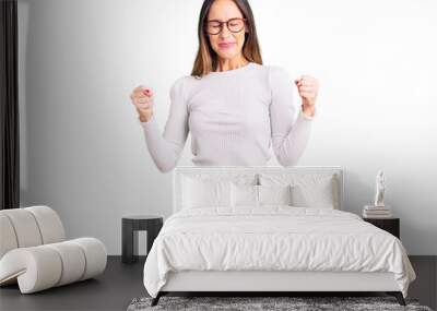 Beautiful brunette young woman wearing casual white sweater and glasses excited for success with arms raised and eyes closed celebrating victory smiling. winner concept. Wall mural