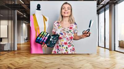 Beautiful caucasian woman dressmaker designer holding scissors and sewing kit smiling and laughing hard out loud because funny crazy joke. Wall mural