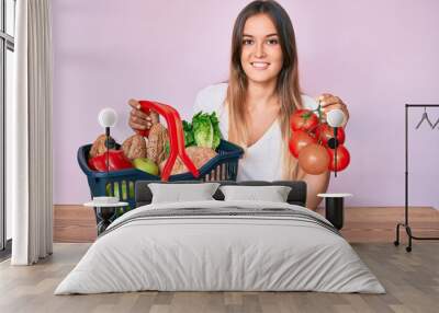 Beautiful caucasian woman holding supermarket shopping basket and tomatoes smiling with a happy and cool smile on face. showing teeth. Wall mural