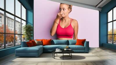 Beautiful caucasian woman wearing sportswear smelling something stinky and disgusting, intolerable smell, holding breath with fingers on nose. bad smell Wall mural