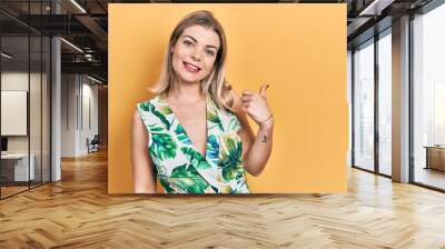 Beautiful caucasian woman wearing summer dress smiling with happy face looking and pointing to the side with thumb up. Wall mural