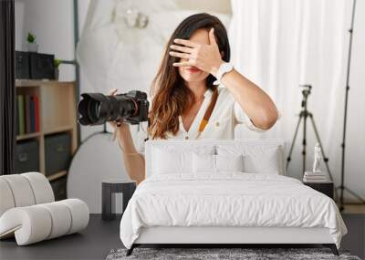 Beautiful caucasian woman working as photographer at photography studio covering eyes with hand, looking serious and sad. sightless, hiding and rejection concept Wall mural