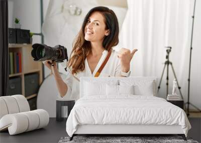 Beautiful caucasian woman working as photographer at photography studio smiling with happy face looking and pointing to the side with thumb up. Wall mural