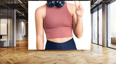 Beautiful caucasian young woman wearing gym clothes and using headphones showing and pointing up with fingers number two while smiling confident and happy. Wall mural