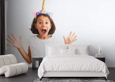 Beautiful child girl wearing unicorn diadem standing over isolated white background celebrating crazy and amazed for success with arms raised and open eyes screaming excited. Winner concept Wall mural