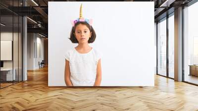 Beautiful child girl wearing unicorn diadem standing over isolated white background Relaxed with serious expression on face. Simple and natural looking at the camera. Wall mural