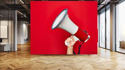 Beautiful hand of man holding megaphone over isolated red background Wall mural