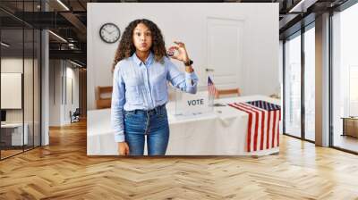 Beautiful hispanic woman standing by at political campaign by voting ballot puffing cheeks with funny face. mouth inflated with air, crazy expression. Wall mural