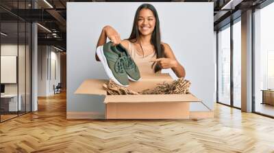 Beautiful hispanic woman taking sneaker shoes from box smiling happy pointing with hand and finger Wall mural