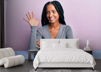 Beautiful hispanic woman wearing casual clothes sitting on the table showing and pointing up with fingers number five while smiling confident and happy. Wall mural