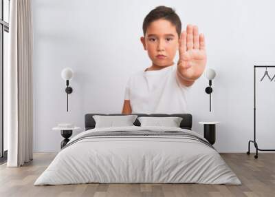 Beautiful kid boy wearing casual t-shirt standing over isolated white background doing stop sing with palm of the hand. Warning expression with negative and serious gesture on the face. Wall mural