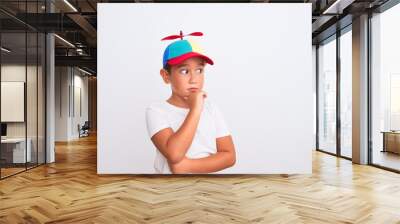 Beautiful kid boy wearing fanny colorful cap with propeller over isolated white background with hand on chin thinking about question, pensive expression. Smiling with thoughtful face. Doubt concept. Wall mural