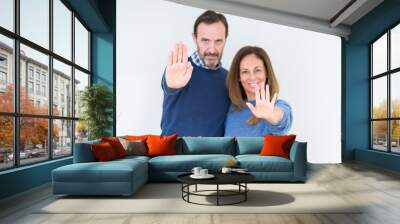 Beautiful middle age couple in love over isolated background doing stop sing with palm of the hand. Warning expression with negative and serious gesture on the face. Wall mural